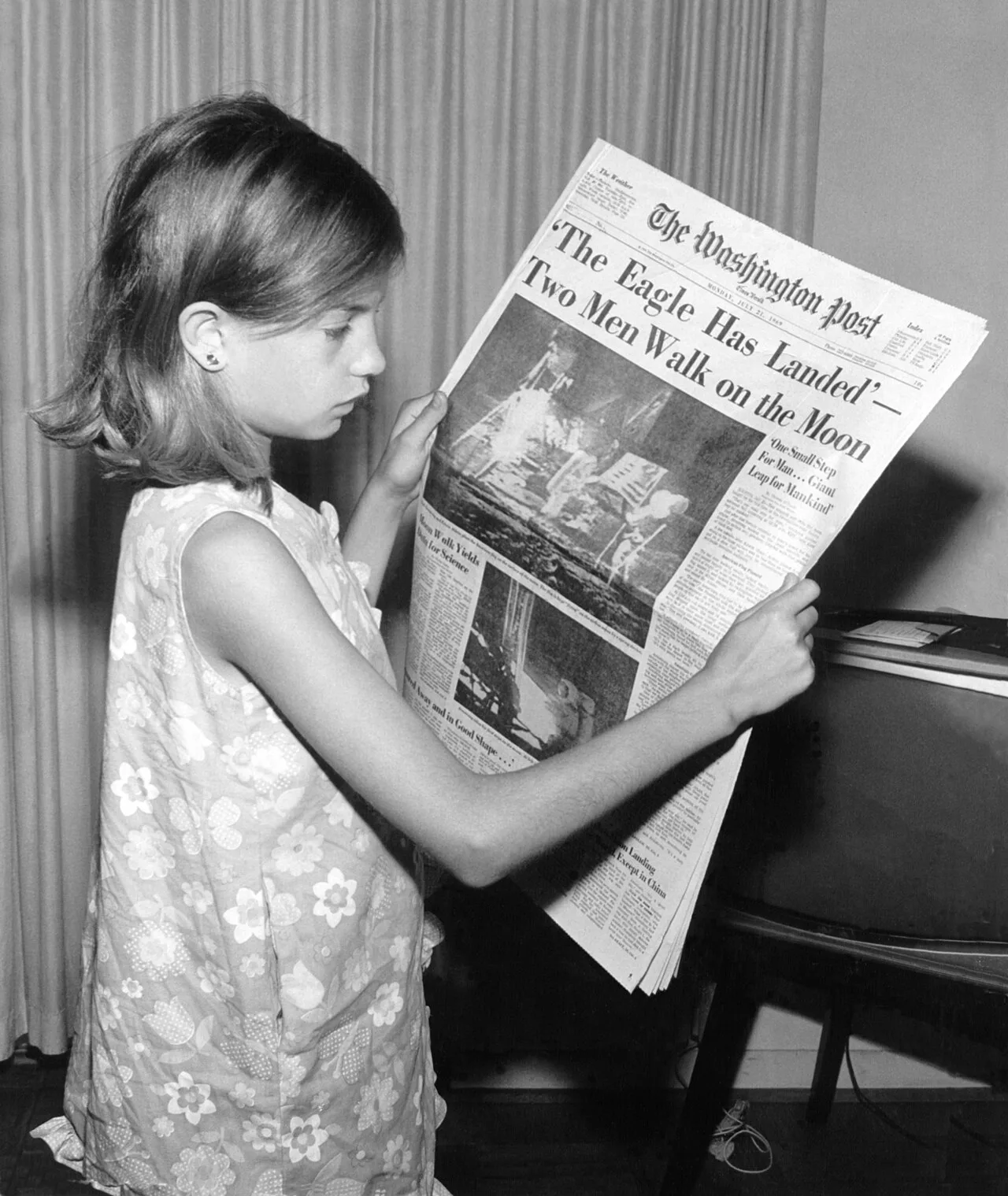 A girl holding The Washington Post newspaper stating "'The Eagle Has Landed' – Two Men Walk on the Moon"
