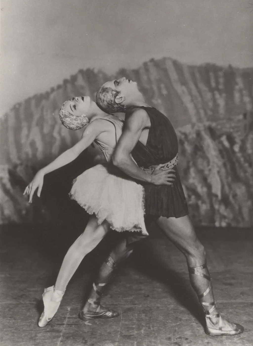 Two dancers pose in front of a rocky background